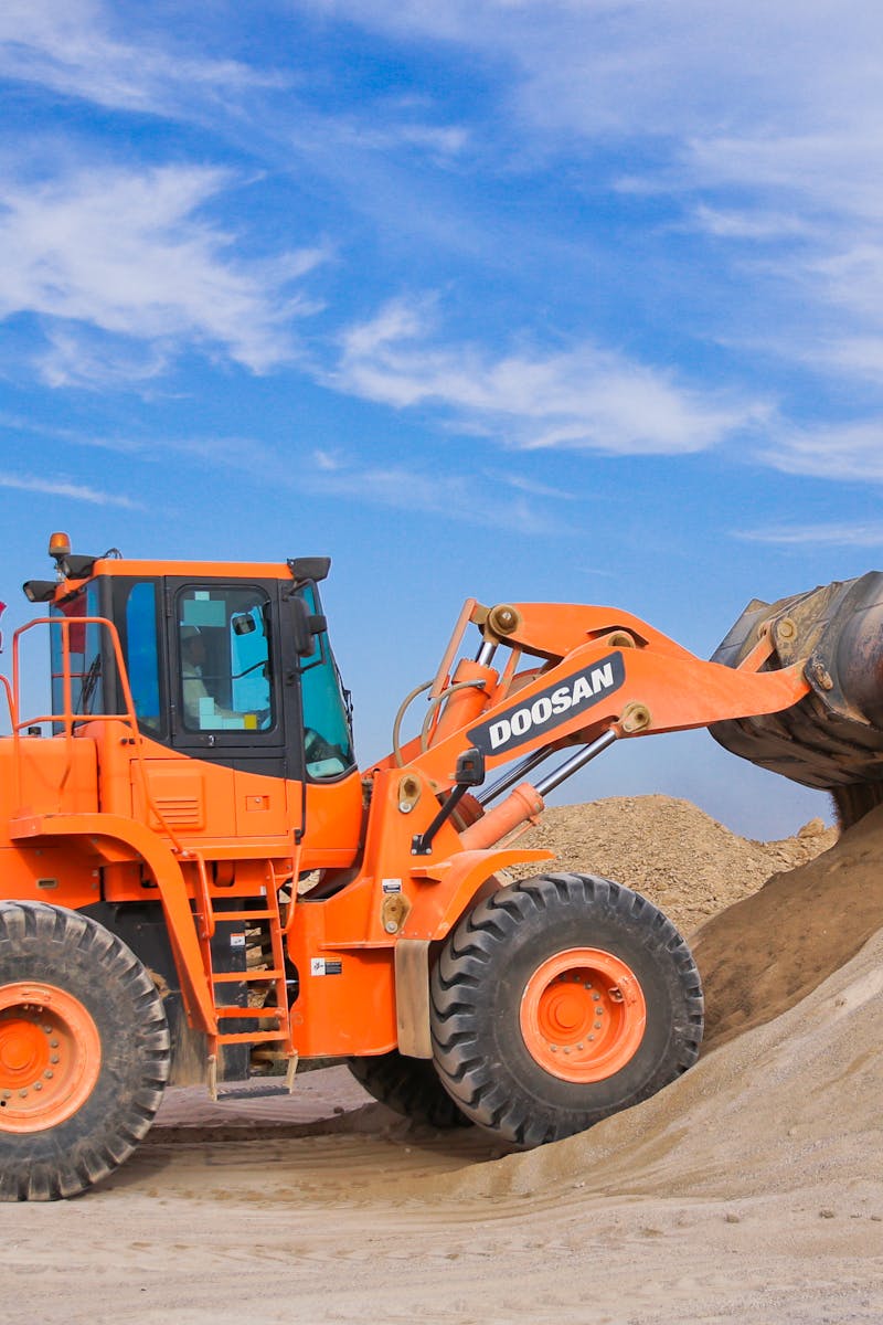 An orange bulldozer at work, moving sand under a clear blue sky on a construction site.